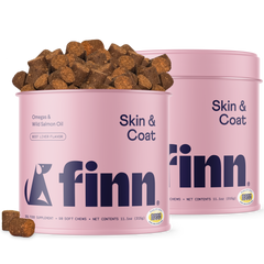 Two pink cylindrical containers of Finn Skin & Coat dog supplements with brown chew treats scattered around and spilling from one container.
