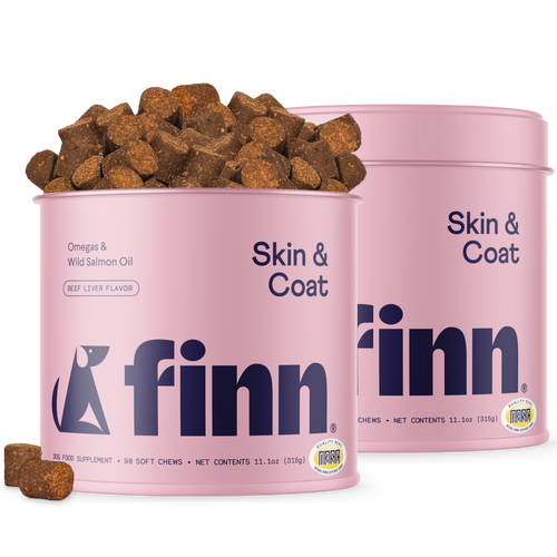 Two pink cylindrical containers of Finn Skin & Coat dog supplements with brown chew treats scattered around and spilling from one container.