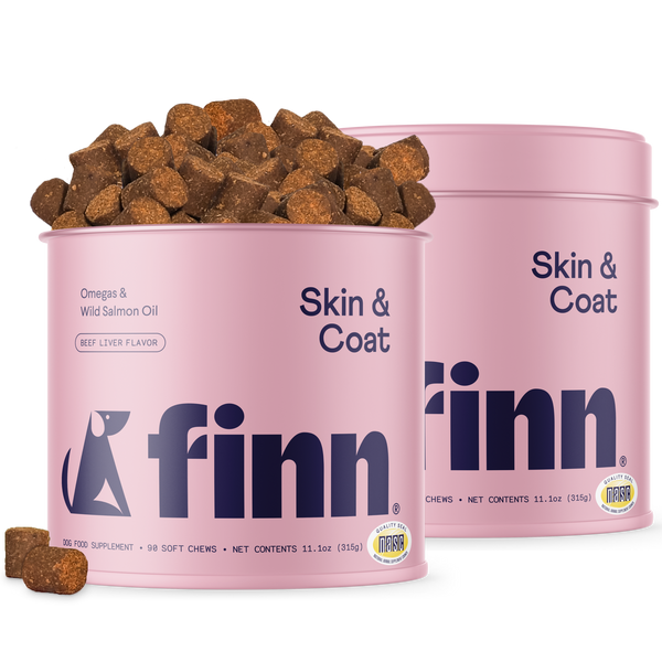 Two pink cylindrical containers of Finn Skin & Coat dog supplements with brown chew treats scattered around and spilling from one container.