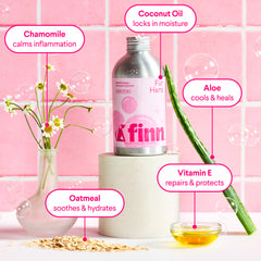 Pink-toned product display showing Finn skincare bottle with natural ingredients: chamomile flowers, oatmeal, aloe vera, and vitamin E oil with benefit labels