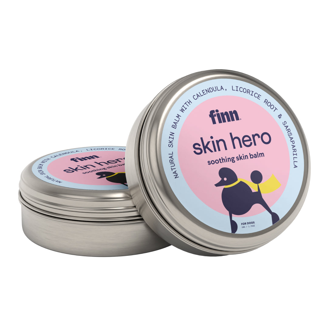 Two round metal tins of Finn Skin Hero soothing skin balm for dogs, featuring pink and blue labels with black dog illustration