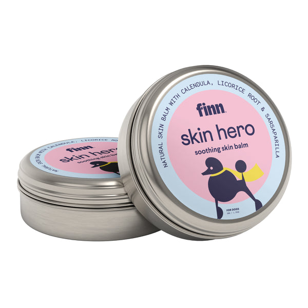 Two round metal tins of Finn Skin Hero soothing skin balm for dogs, featuring pink and blue labels with black dog illustration