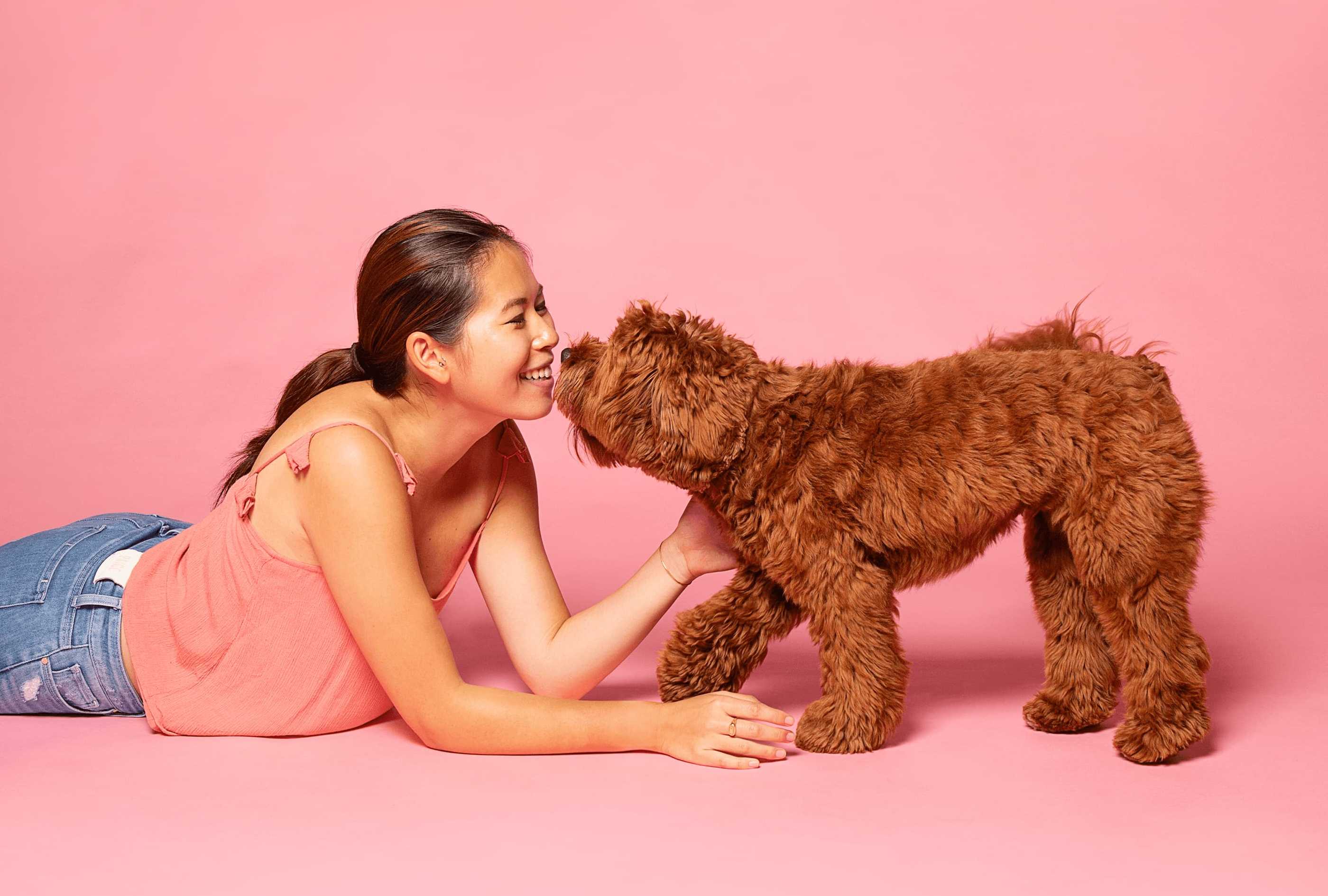Woman lying on a pink floor with a brown dog, both looking at each other.