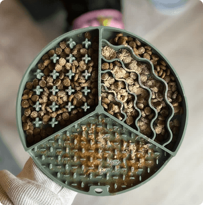 Round green silicone lick mat with three sections containing different textured patterns and brown treats or kibble