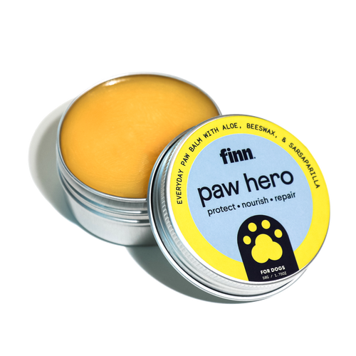 Open tin of yellow paw balm with blue and yellow label reading "finn. paw hero protect • nourish • repair" with paw print logo