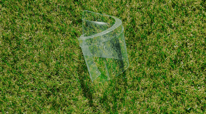 Clear plastic container or cup lying on green grass, appearing discarded as litter in an outdoor setting.