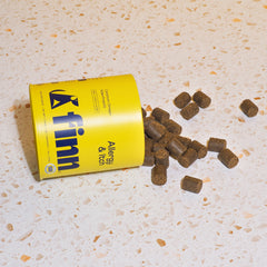 Yellow FINN dog food can tipped over with brown kibble pellets spilled on speckled countertop
