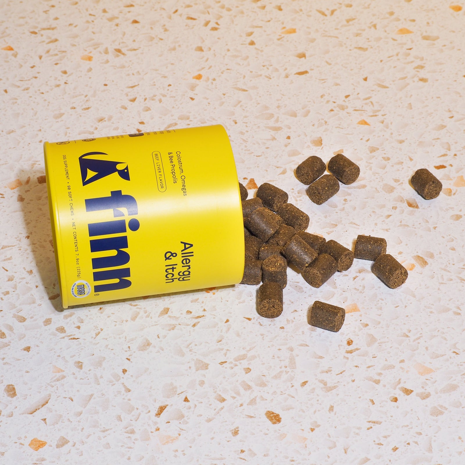 Yellow FINN dog food can tipped over with brown kibble pieces scattered on speckled beige surface