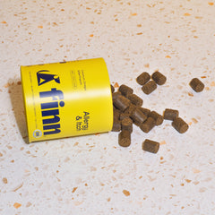 Yellow FINN dog food can tipped over with brown kibble pieces scattered on speckled beige surface